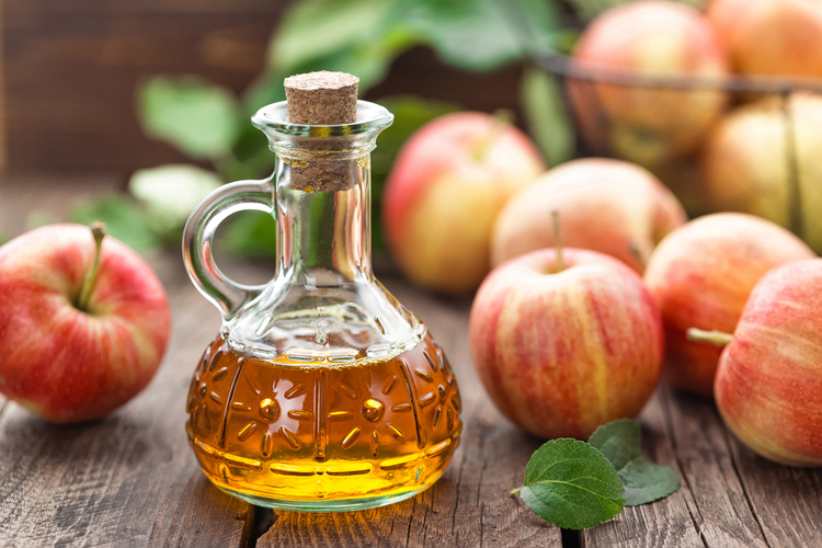 Apple cider vinegar with several apples on a wooden surface.