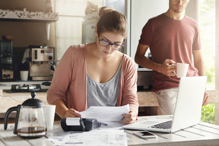 Young woman doing accounts together with her husband at home, budgeting.