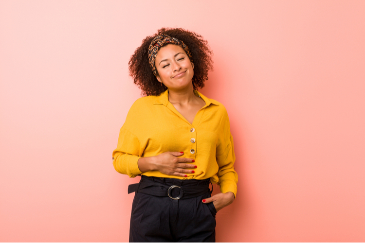 Woman against a pink background touches tummy showing good digestion.