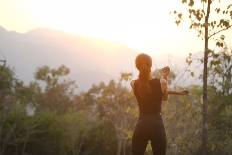 Rear view healthy young woman stretching in the park before running at the sunset.
