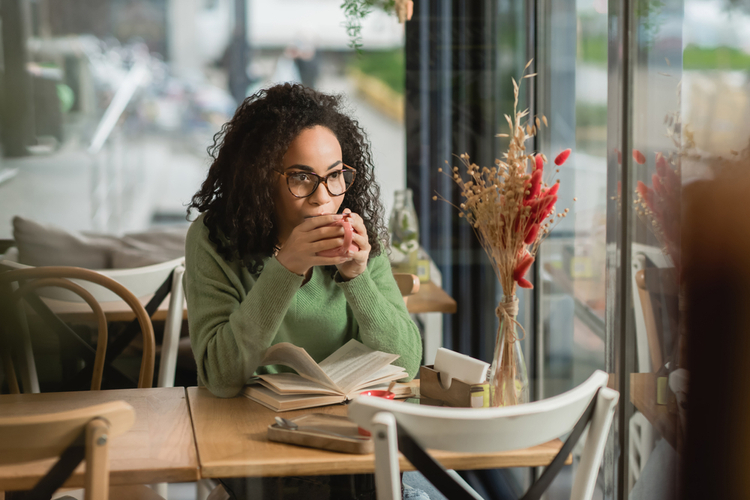 Woman in eyeglasses and book drinking coffee in cafe