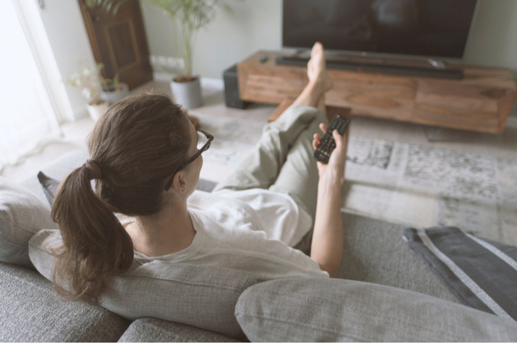 Woman relaxing on the sofa at home and holding a remote.