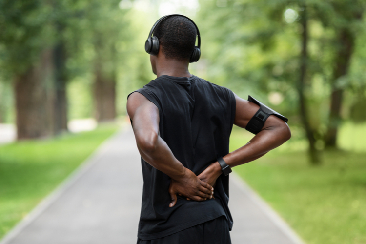 Man in sportswear standing in park and touching injured back needing abdominal exercises.