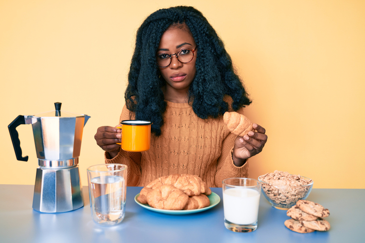 Woman eating breakfast holding croissant depressed.