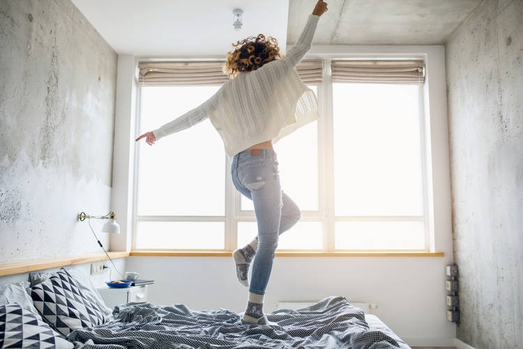 Attractive woman jumping on bed in after she eats breakfast the morning.