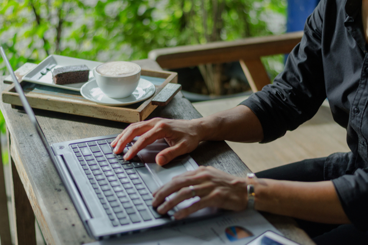 Freelancer using laptop computer working on part-time job while drinking coffee.