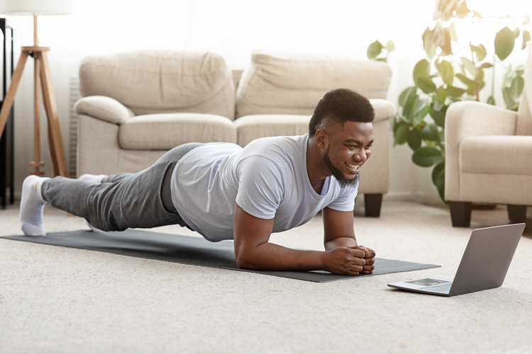 Man doing yoga plank while watching online tutorial on laptop.