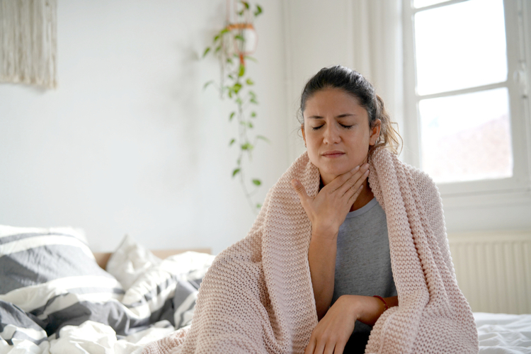 A woman with sore throat sitting on the bed.