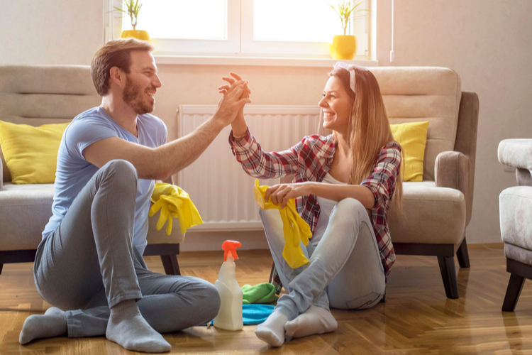 Couple is giving high five and smiling while sitting on the floor in living room after cleaning it.