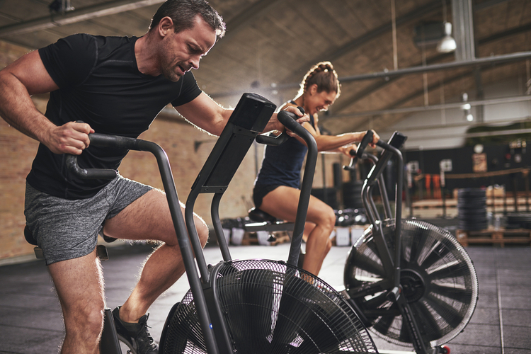 Young man and woman wearing training hardly on cycling machines in light spacious gym.