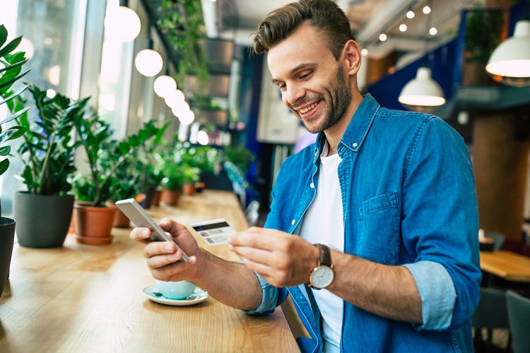 Man with credit card and phone in hands doing purchases during online shopping.