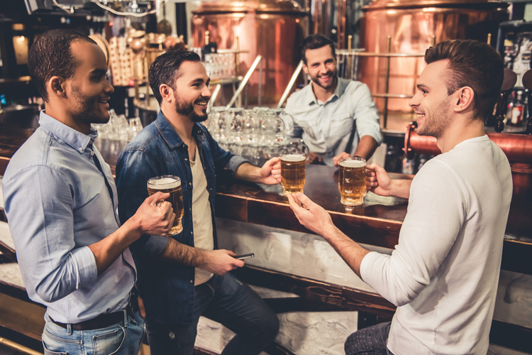 Group of guys are drinking beer, talking and smiling while resting in pub.