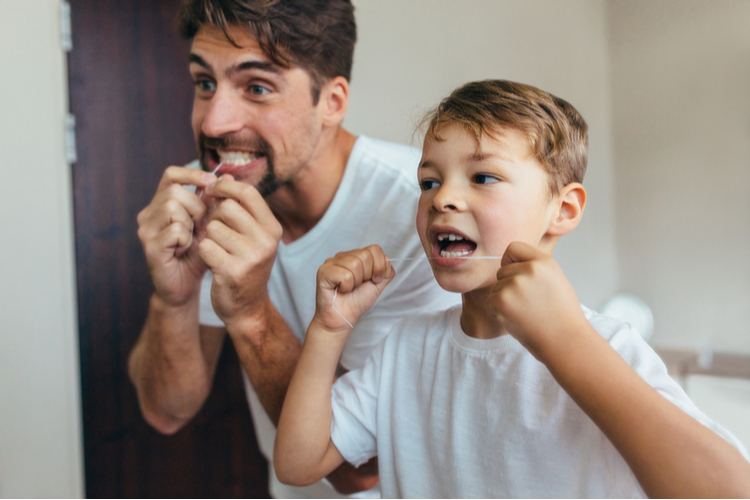 Father and son flossing their teeth in the bathroom.