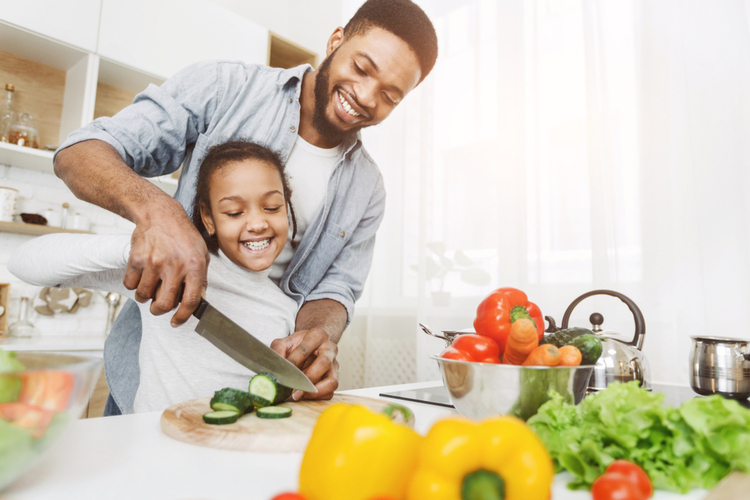 Man teaching his little daughter to cut vegetables.