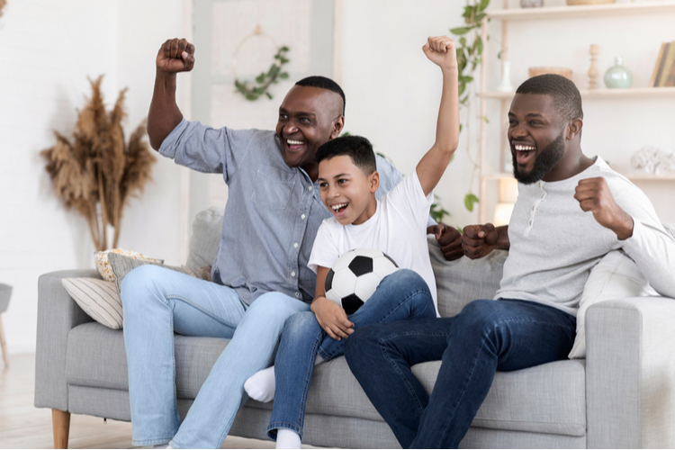 Excited grandfather, dad and son cheering favorite football team at home.