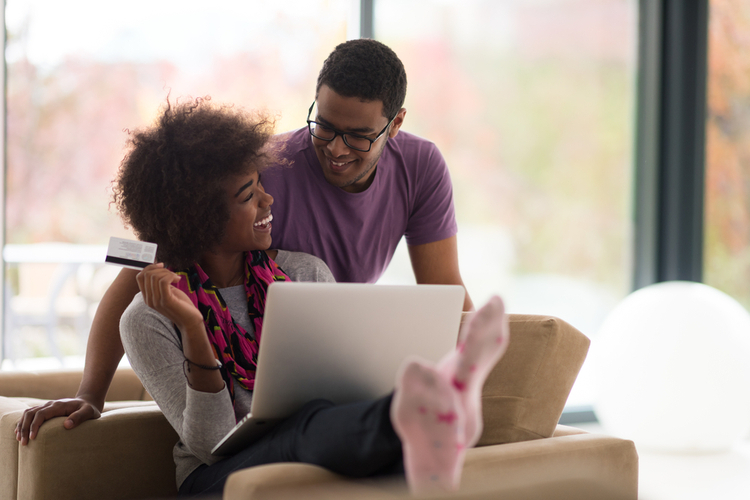 Couple shopping online through laptop using credit card at home.
