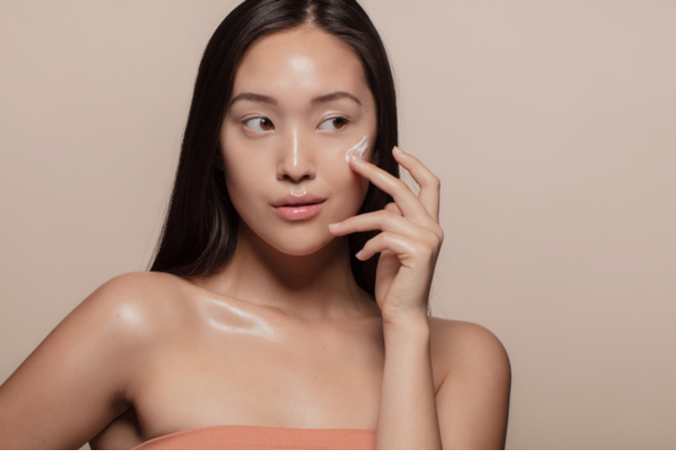 Woman applying loum beauty of calm to her face over beige background.