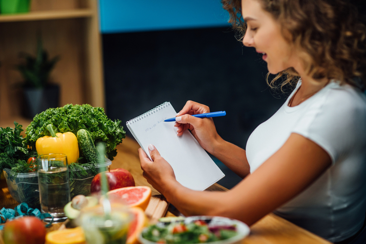 Woman writing diet plan on table and using vegetables.