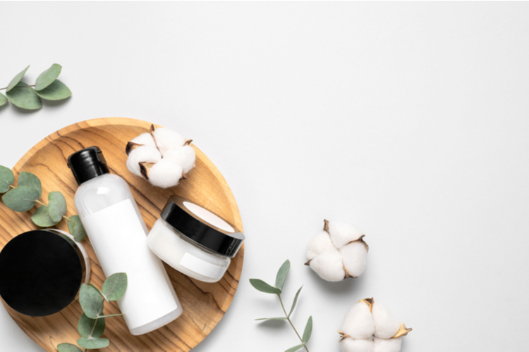 Cosmetic containers with cream and lotion, cotton flowers, eucalyptus leaves.