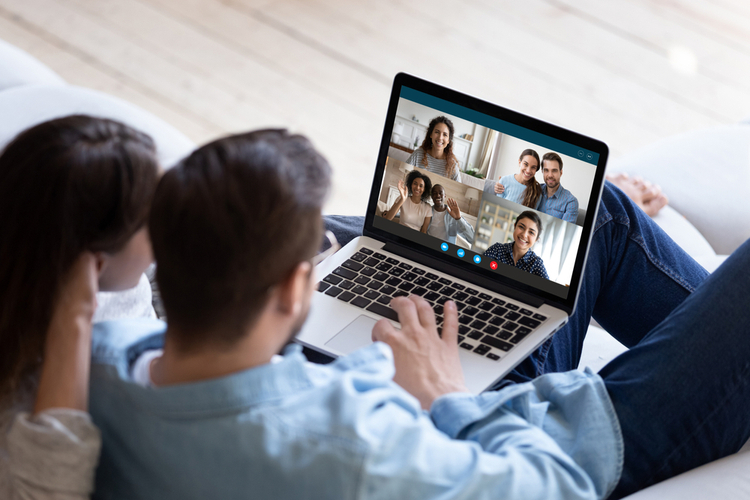 Back view of young couple relax on couch speak talk on video call with multiracial friends as a practice for mental wellbeing during COVID.