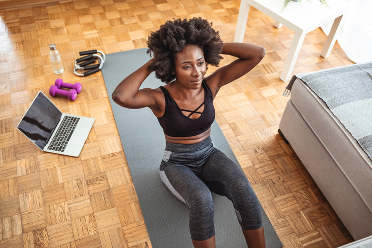 Young fit woman in black sportswear is doing sit-ups at home for spot fat reduction on her abdomen.
