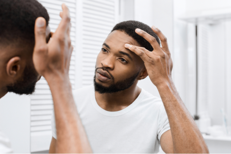 Man touching his face, looking herself in mirror in bathroom.