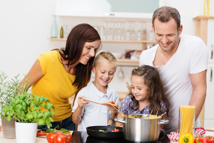 Happy young family with Mom and Dad and two young children cooking in the kitchen.