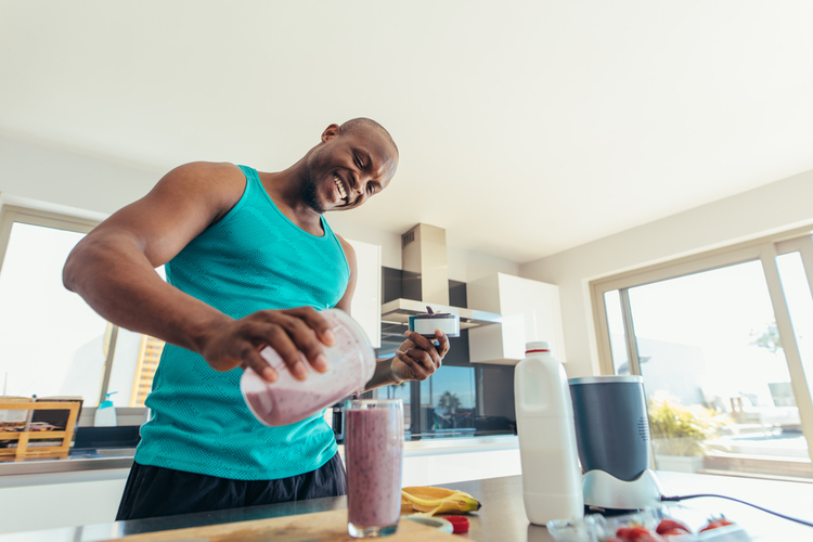 Smiling man pouring milkshake in a glass for drinking.