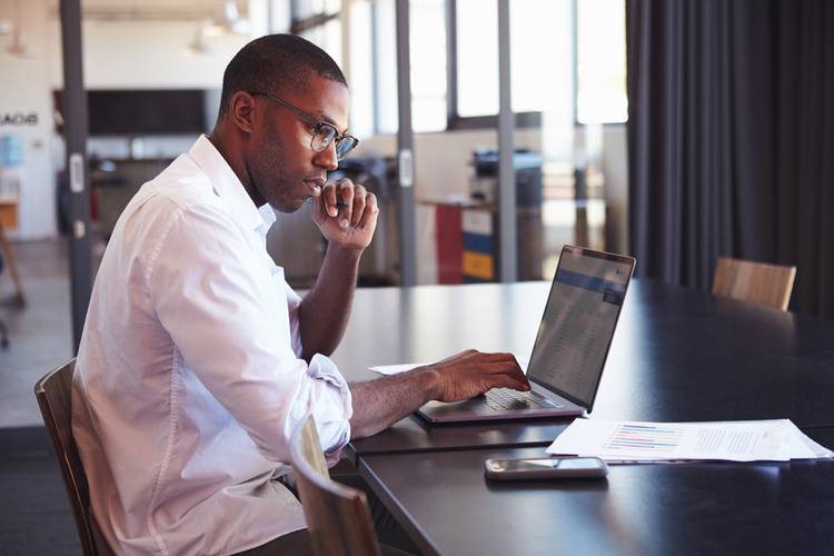 Man wearing glasses using laptop in office.