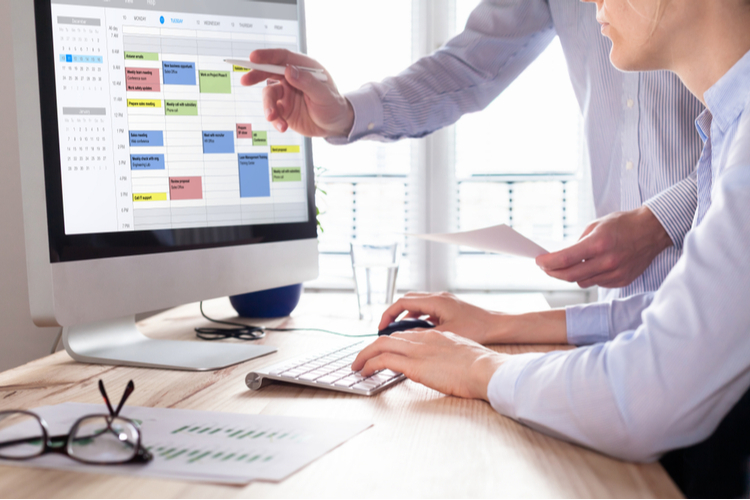 Colleagues planning a meeting with calendar software on computer.