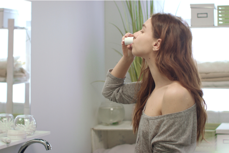 Young woman rinsing mouth with teeth rinse front mirror in bathroom before sleep. Healthy woman using dental rinse while morning care in bath room.