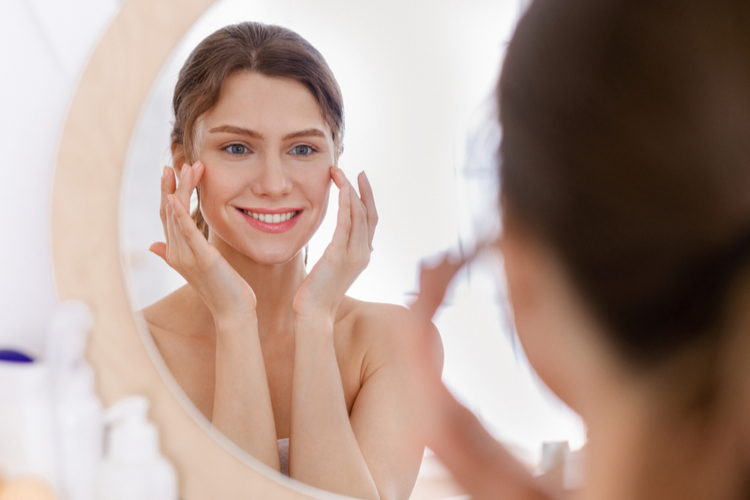 Beautiful smiling woman looking at mirror using bota serum.