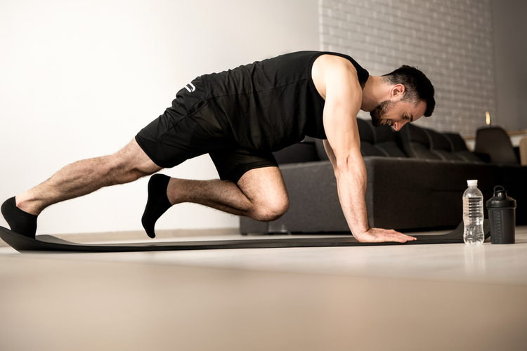 Man doing mountain climber exercises on black yoga mat.