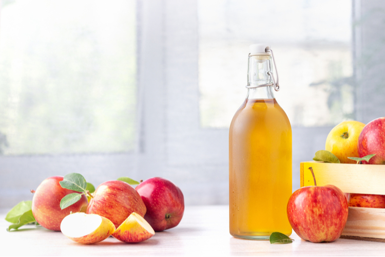 Apple cider vinegar in glass bottle and fresh red apples on a light background.