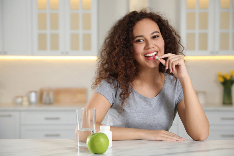 Woman taking vitamin pill in kitchen.