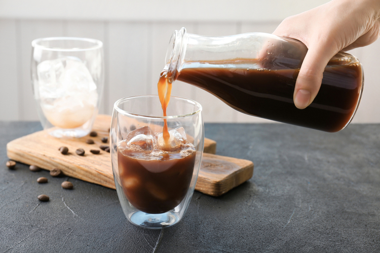 Woman pouring cold brew black coffee into glass on table.