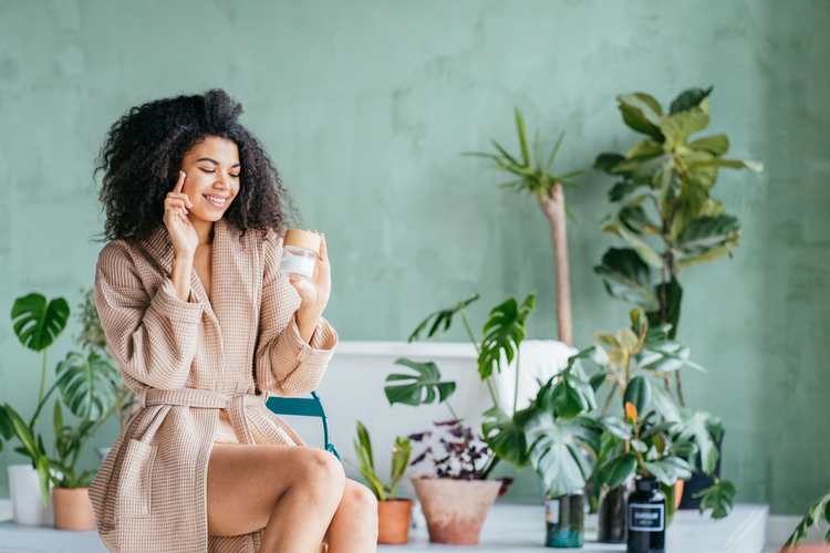 Young woman in bathrobe apply cream on face using eco-friendly product.