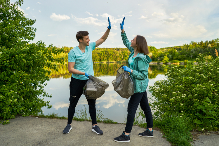 Friends crouching with bag picking up trash doing plogging. Plogging concept. Boy and girl picking up trash from the forest. They collecting the litter in garbage bag