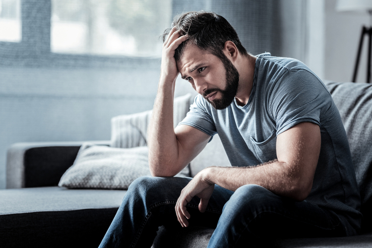 Sad unhappy handsome man sitting on the sofa and holding his forehead.