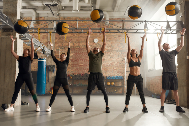 Group of fit individuals using exercise ball while having workout at industrial gym.