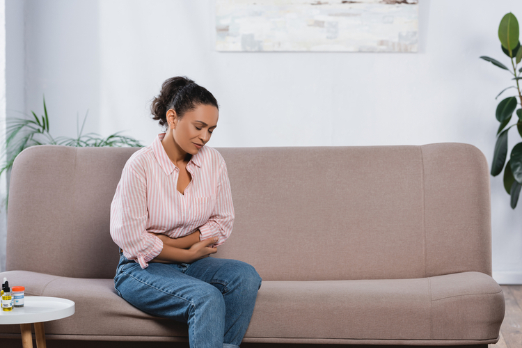 Woman suffering from abdominal pain in living room about to use original hemp daily dose tinctures.
