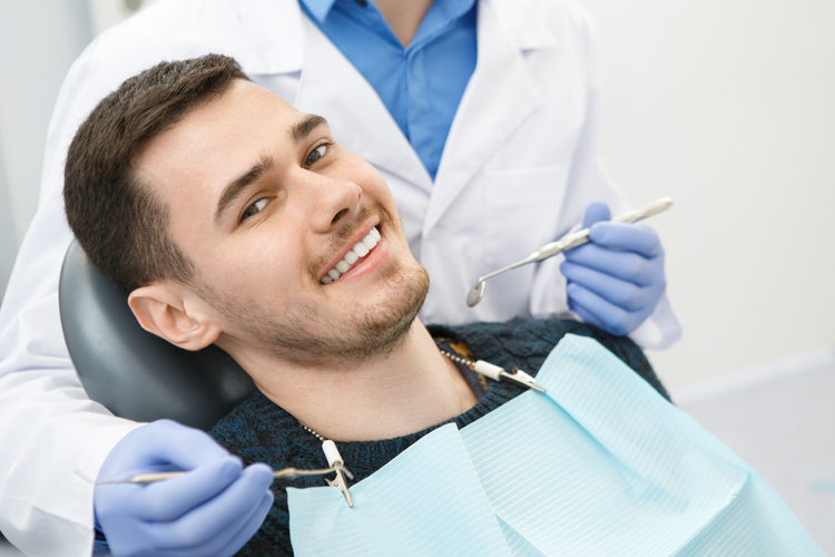 Man smiling to the camera sitting in a dental chair with his dentist preparing for dental checkup.
