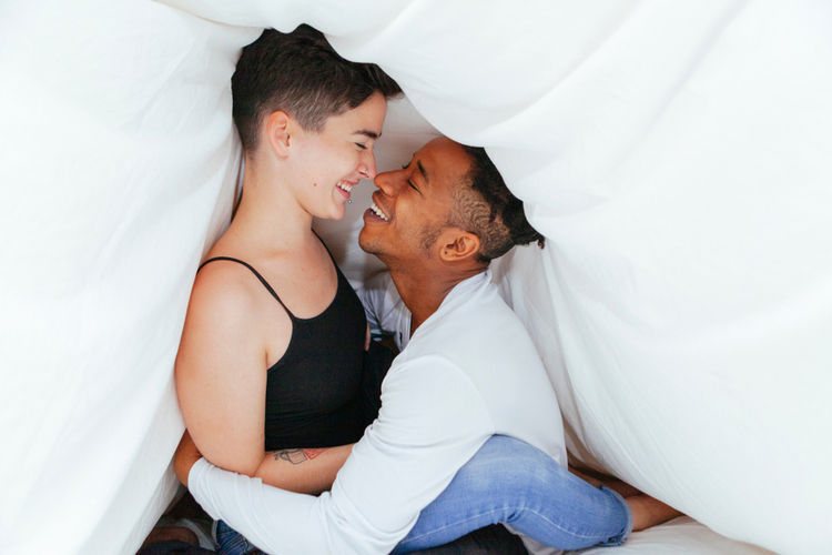 Cheerful casual couple playing tickles under the bed cover know what is sexual health.