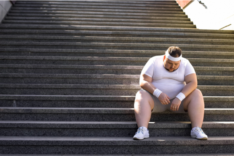 Overweight man sitting on stairs after jogging losing motivation.