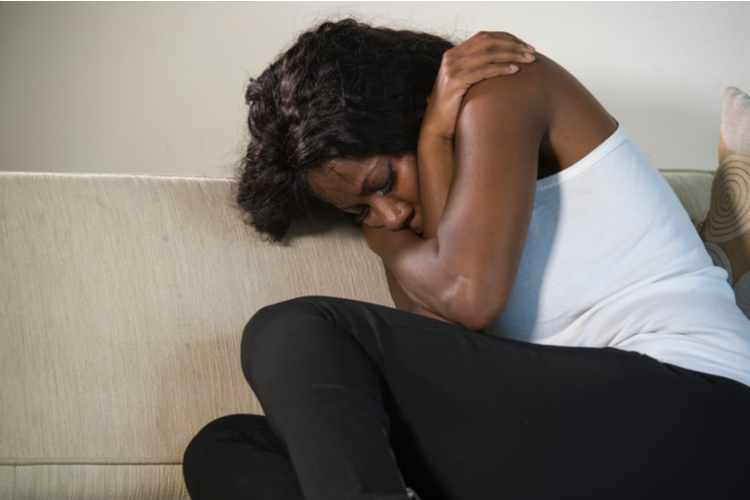 African American hugging herself while crying at the sofa.