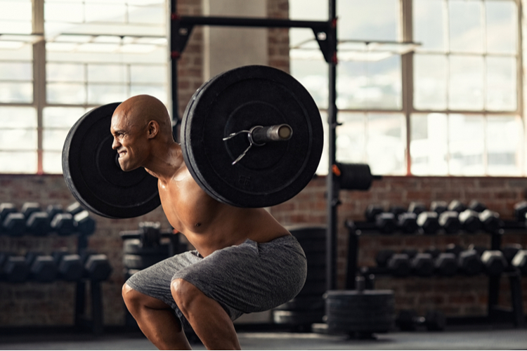 Muscular African-American man taking efforts to lift weight barbell in fitness center, boosting his testosterone levels.