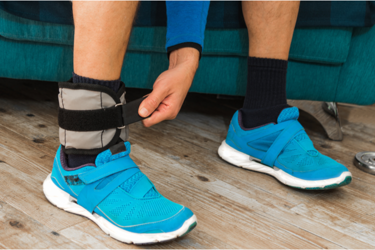 Close up of a man closing velcro strap of an ankle weight during a home workout.