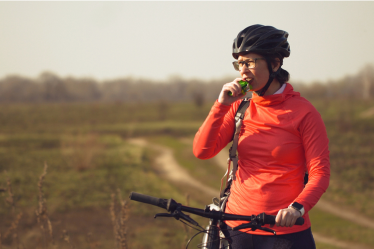 Athletic Caucasian Woman Eats Protein Bar Ride on Mountain Bike on Nature