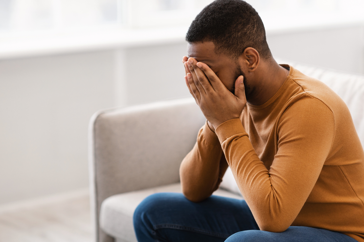 Male Depression. Desperate Depressed African Man Covering Face Crying Having Problems Sitting On Couch At Home.