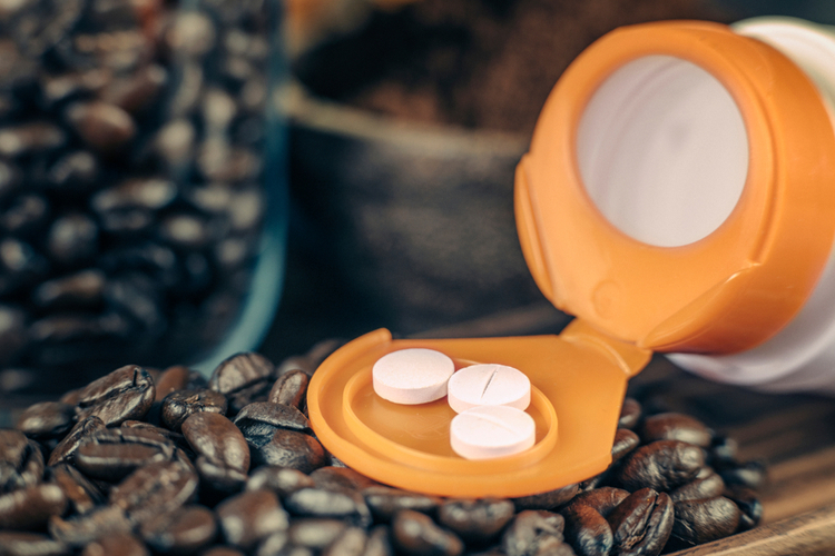 EU Natural Elite Caffeine supplementation bottle with pills and roasted coffee beans on a wooden plate.